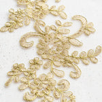 Close up view of light gold corded floral applique embroidered with gold thread and edged with metallic gold cord