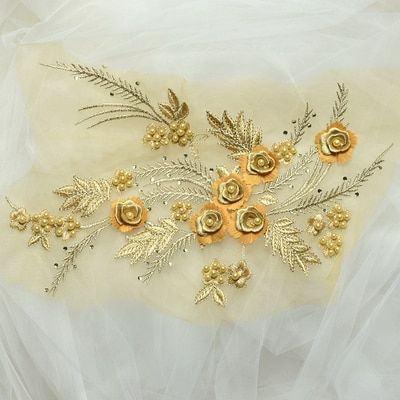 An embroidered gold applique with a floral spray of satin and metallic threads. The  features multi layered embroidered flowers with gold pearl centres and metallic embroidered fern fronds.  The applique is laying flat on white net.
