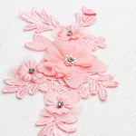 Close up of pink embroidered floral applique with one large and three smaller 3D fabric flowers.  The fabric flowers have crystal centres circled with pearl beads.