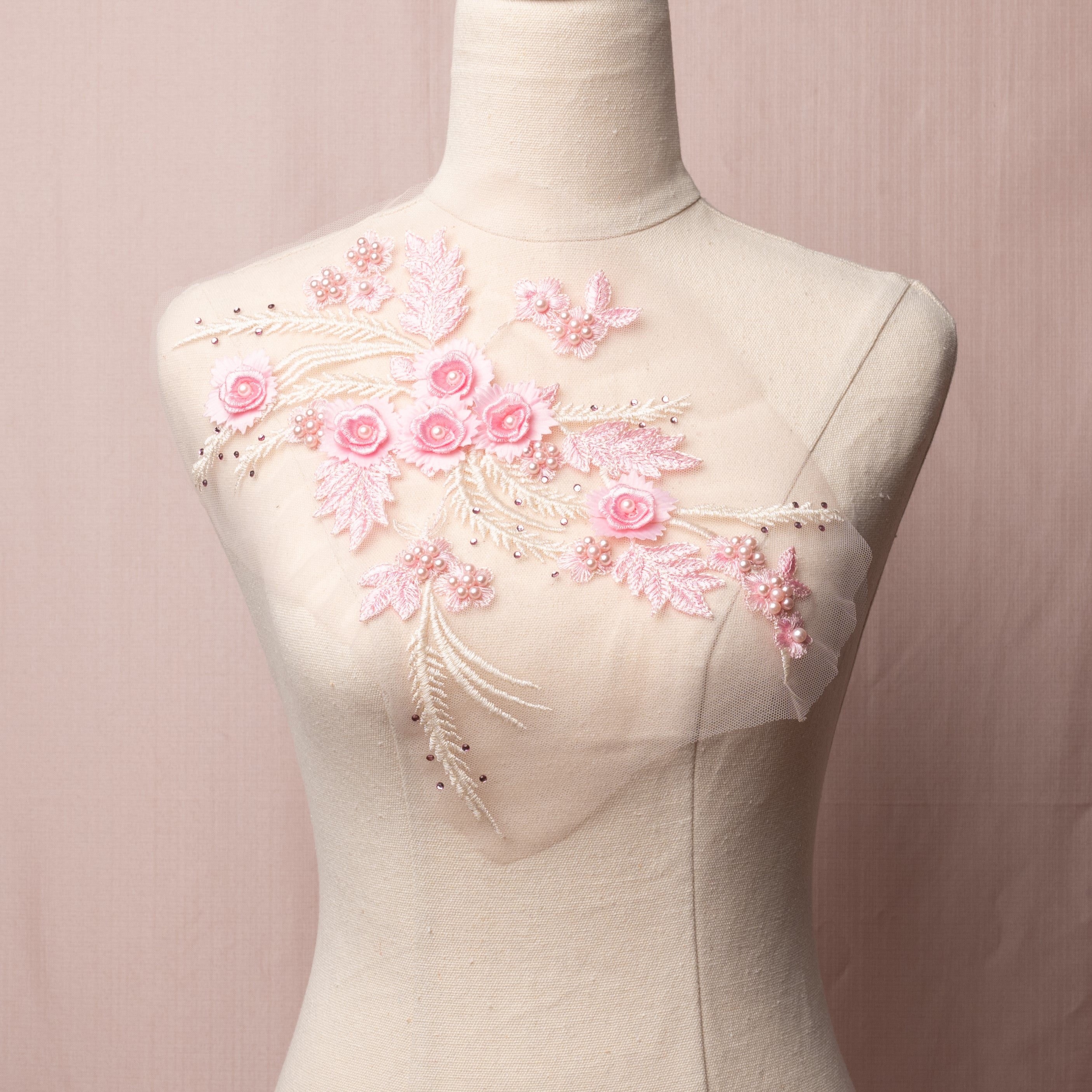 A delicate pale pink mirrored pair with lots of texture combining 3D flowers with pink pearls and a scattering of pink gems embroidered onto a fine net.   The applique is displayed on a mannequin.