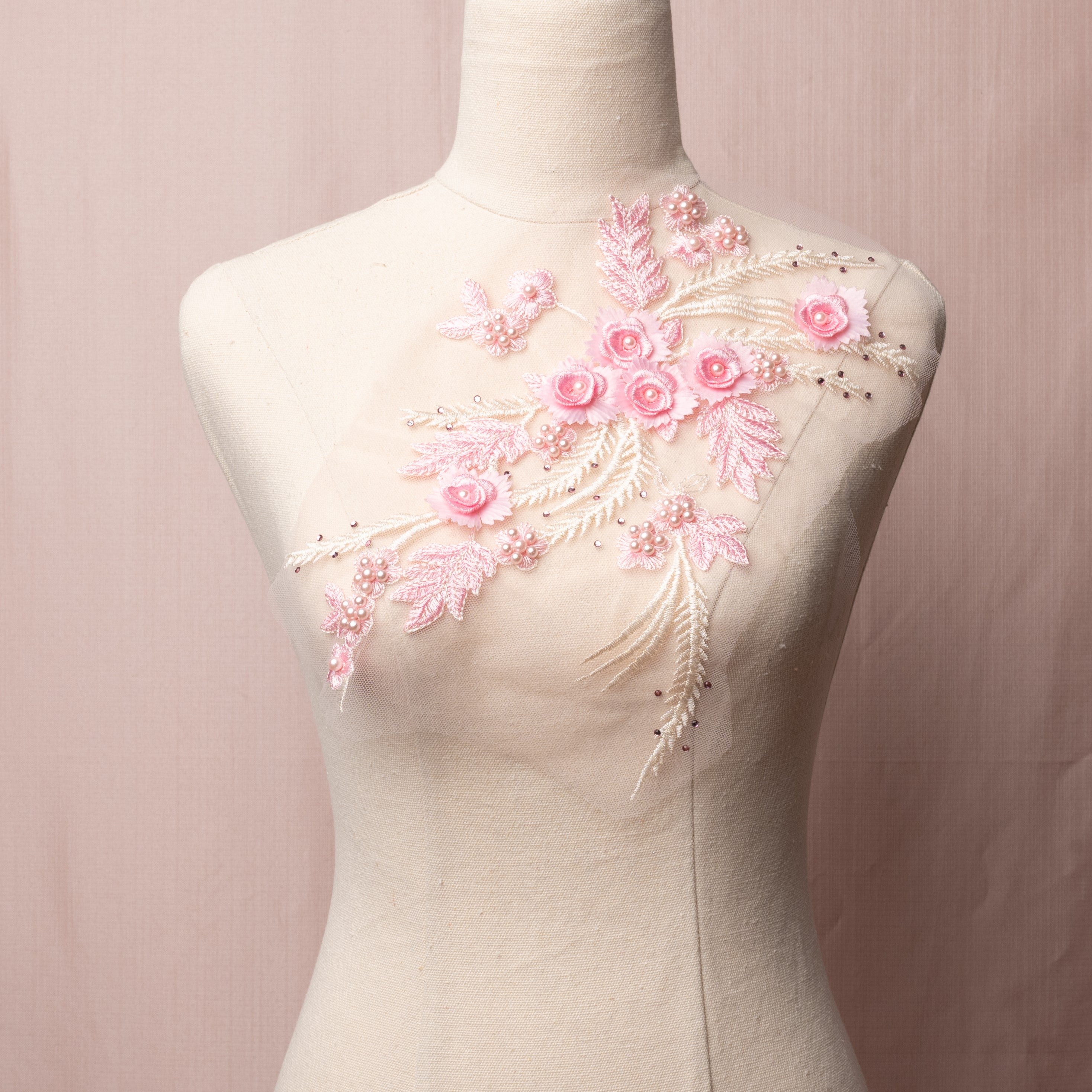 A delicate pale pink mirrored pair with lots of texture combining 3D flowers with pink pearls and a scattering of pink gems embroidered onto a fine net.   The applique is displayed on a mannequin.