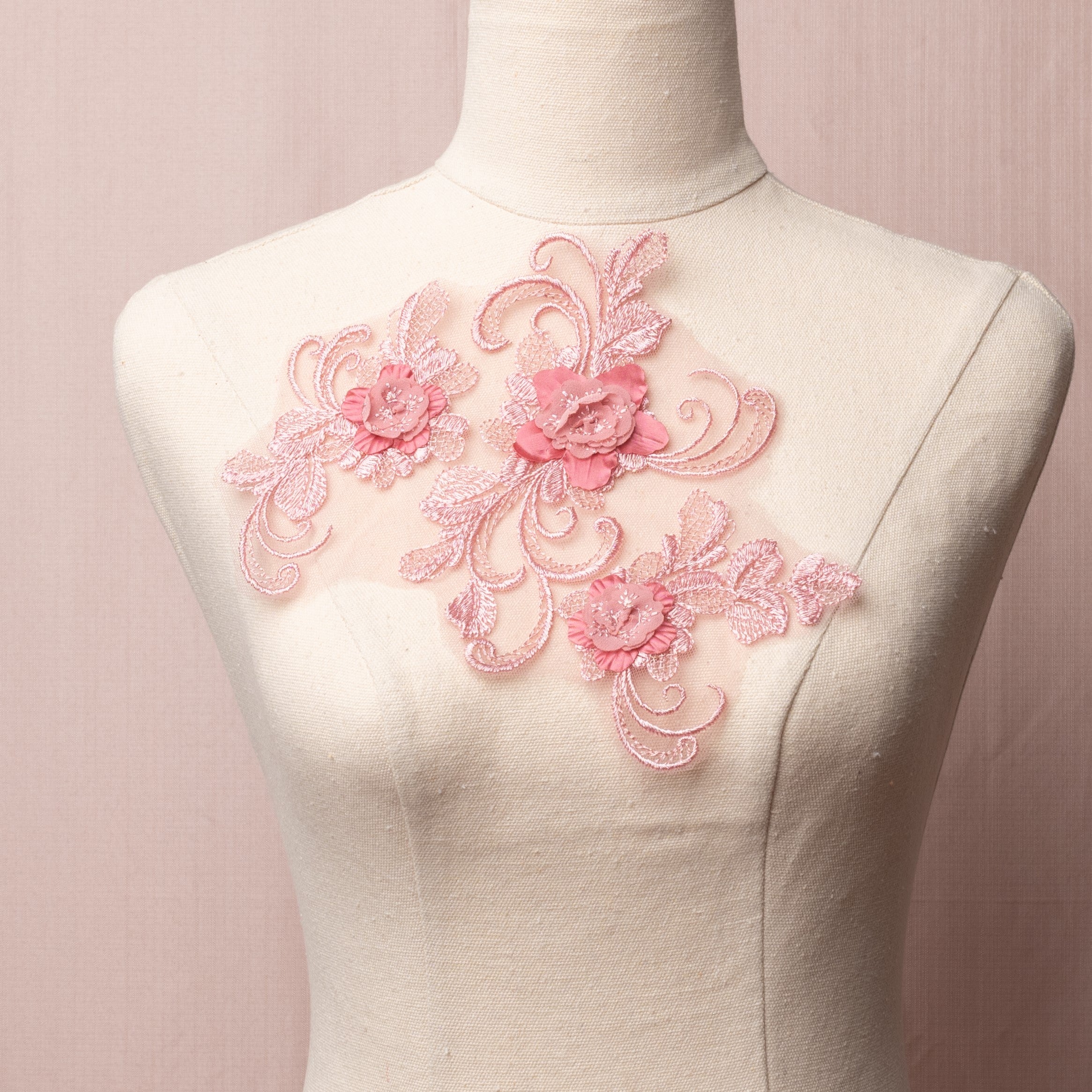 An openwork embroidered dusty pink single applique in a floral design with swirling stems, 3D flowers and crosshatched leaves displayed on a mannequin.