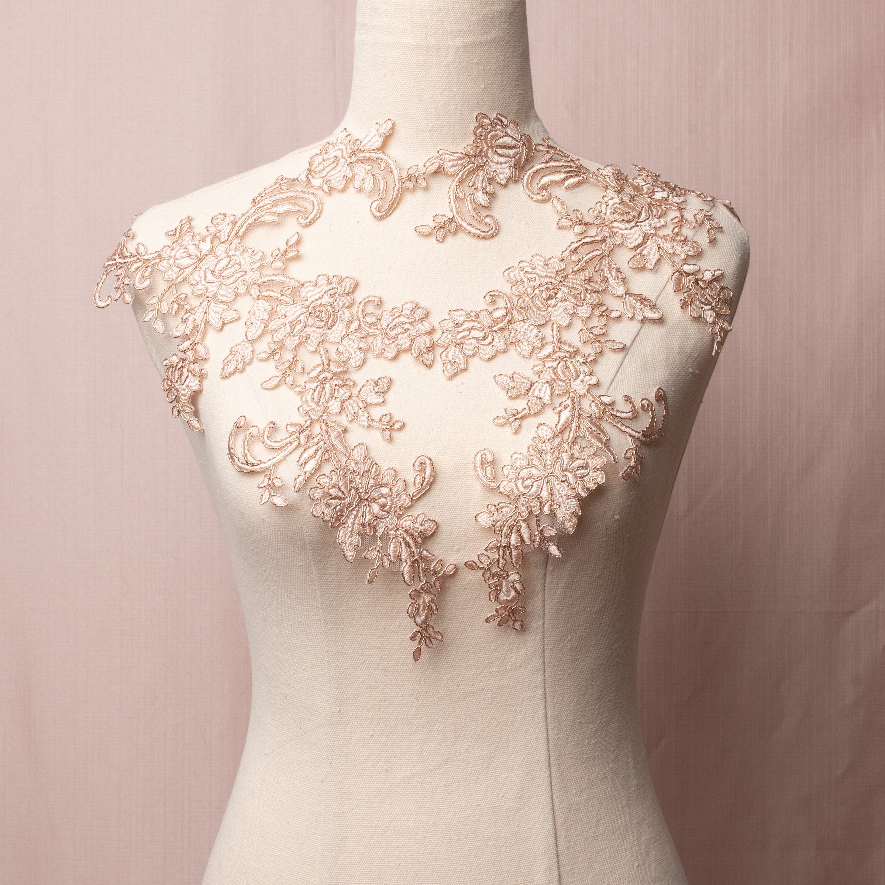 Heavily embroidered rose gold applique with a floral pattern edged with metallic rose gold cording.  The appliques are displayed on a mannequin.