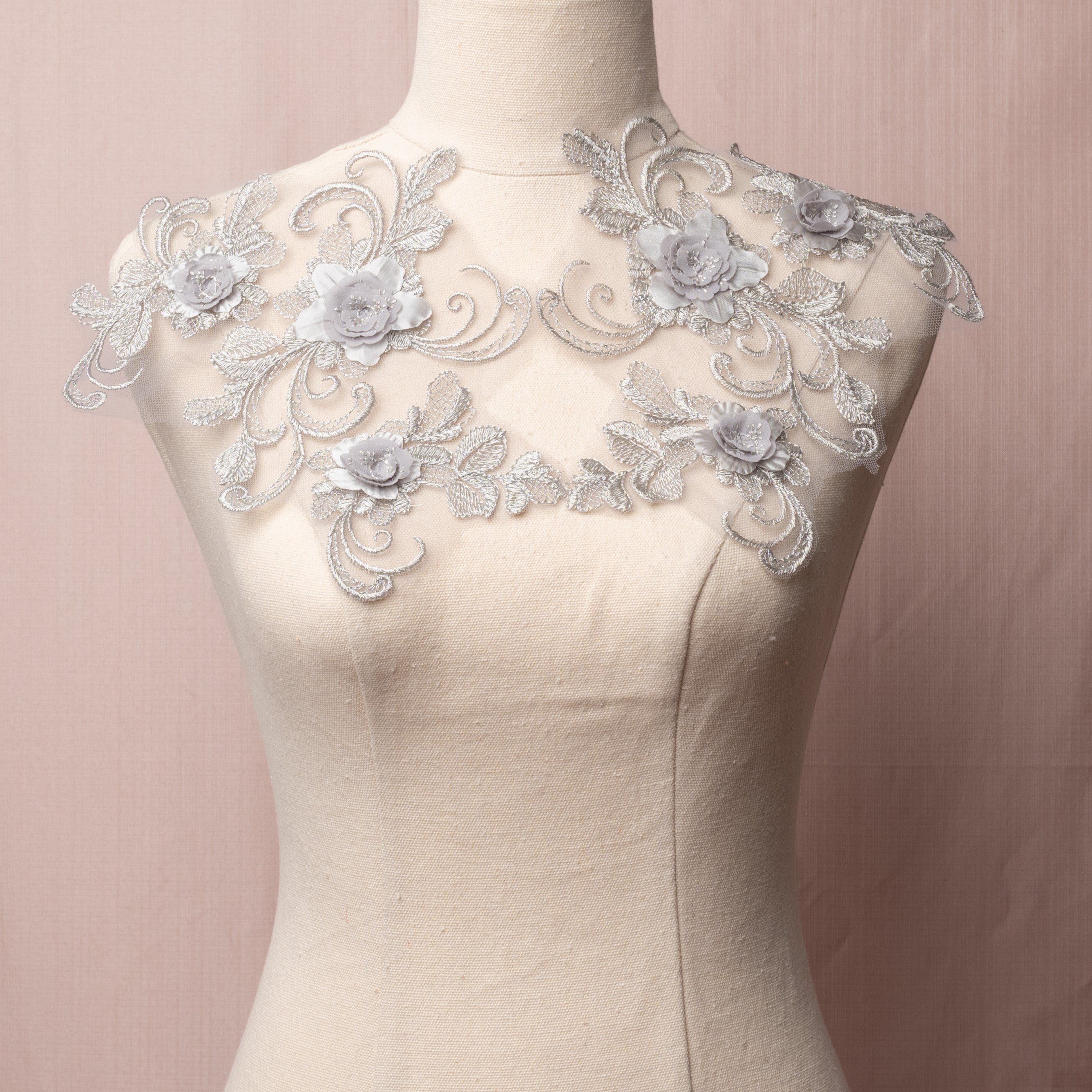 Grey lace applique pair with an open romantic design of swirling stems, cross hatched leaves and 3D rose like flowers.  The appliques are displayed on a mannequin. 