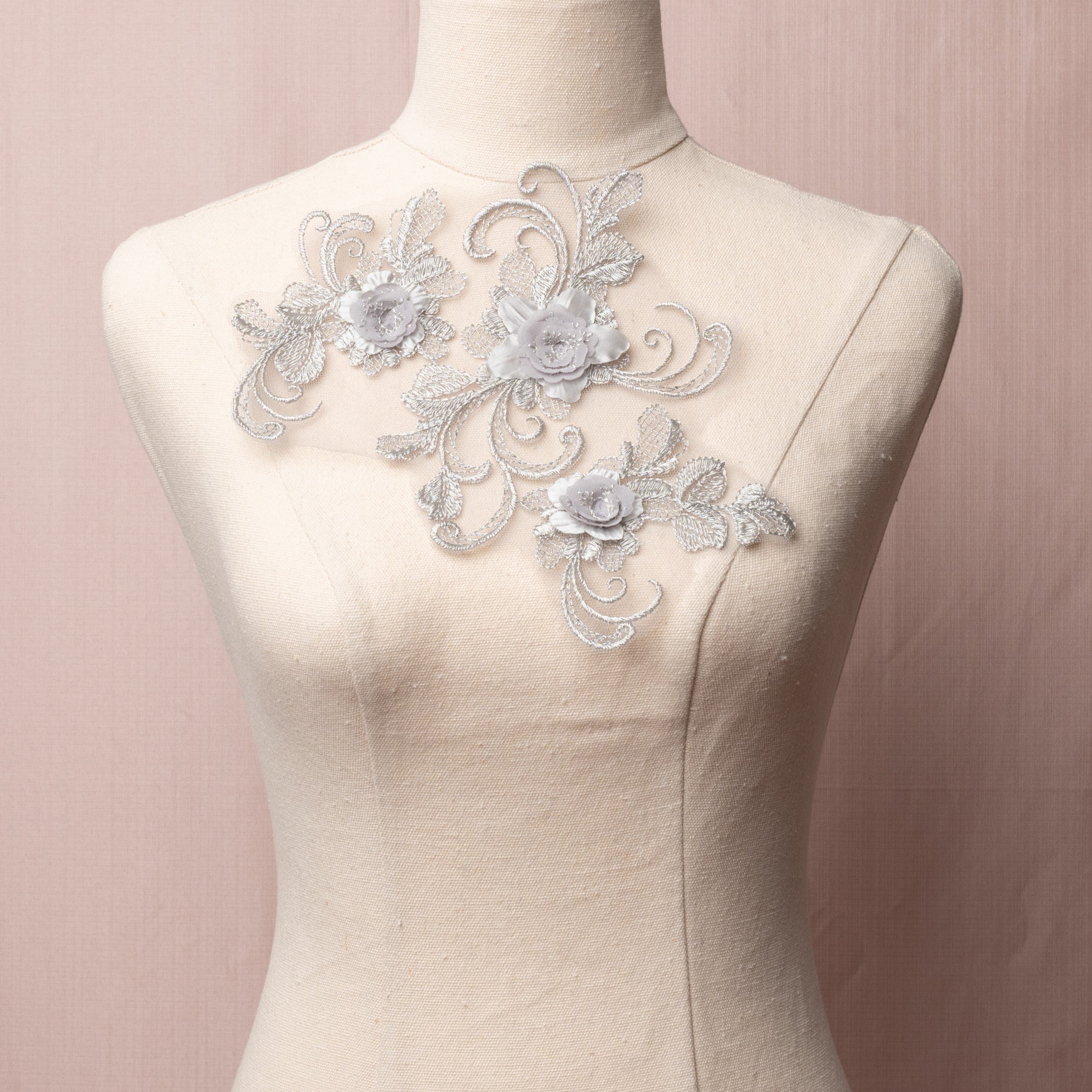 Single grey lace applique with an open romantic design of swirling stems, cross hatched leaves and 3D rose like flowers.  The applique is displayed on a mannequin. 