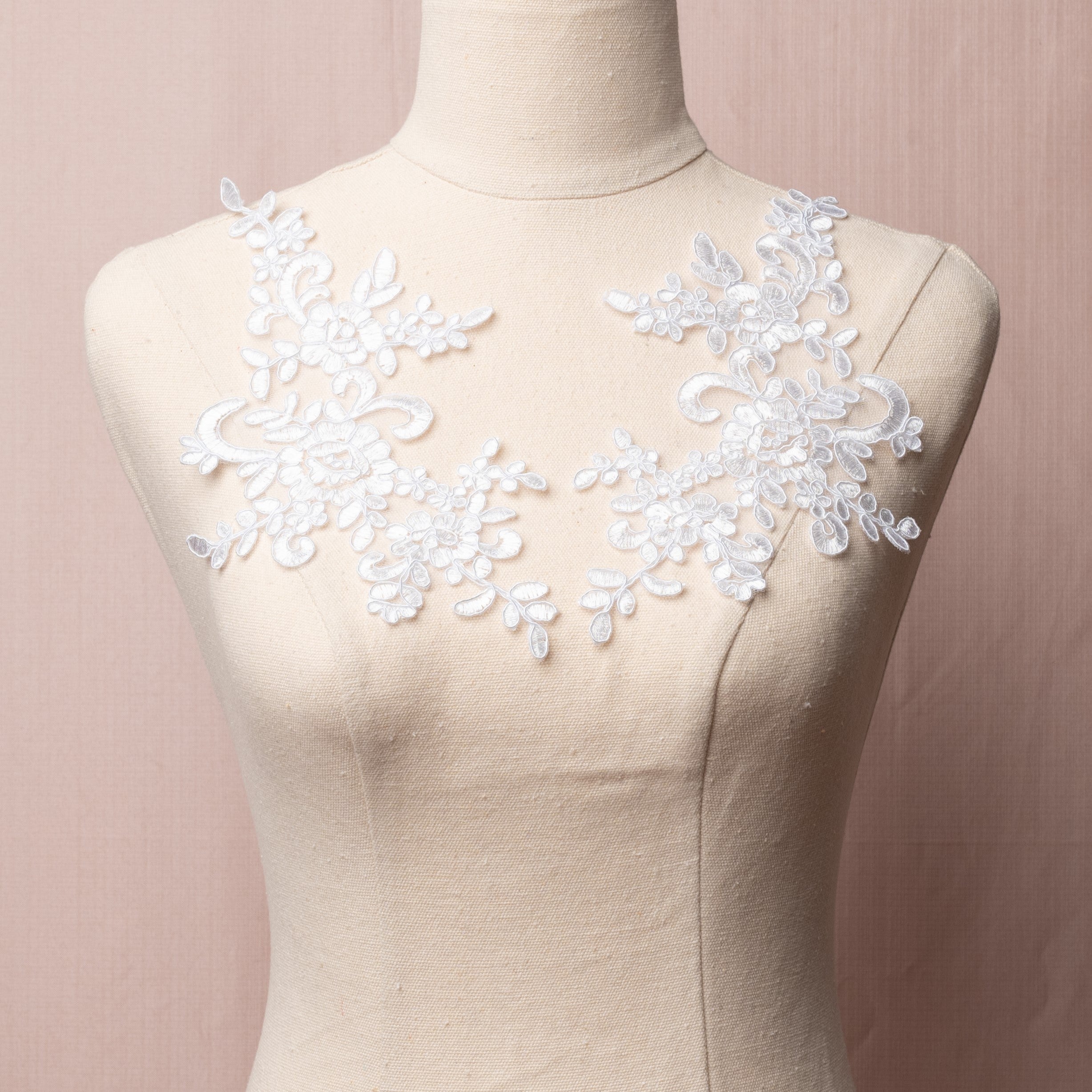 White embroidered and corded applique pair with a floral design.  The appliques are displayed on a mannequin.