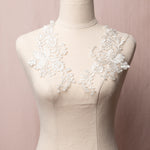 White embroidered floral applique pair edged with silver cord.  The appliques are displayed on a mannequin.