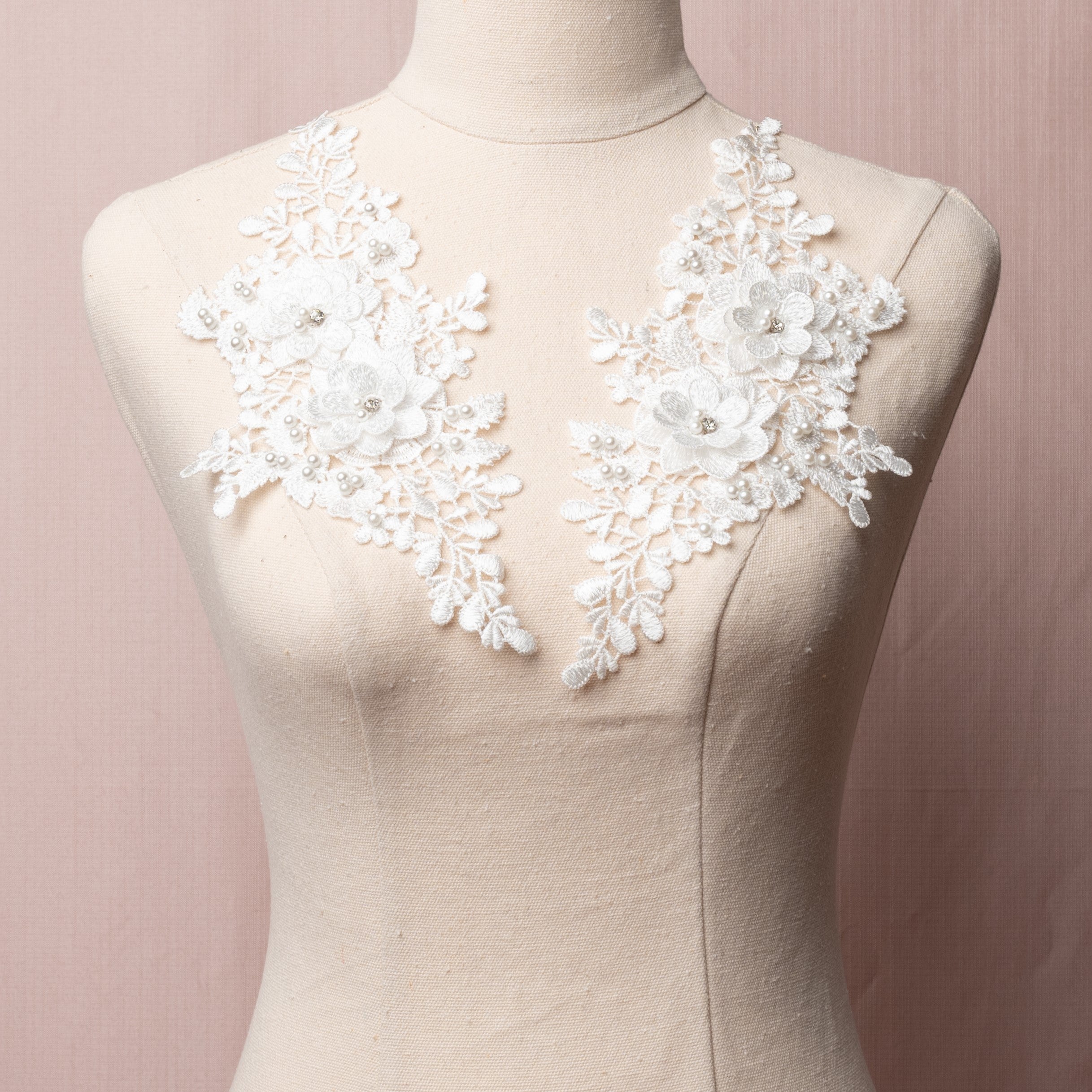 White mirrored pair embroidered applique with 3D flowers.  The applique is embellished with a scattering of white pearls and the 3D flowers have a crystal centre.  The appliques are displayed on a mannequin.