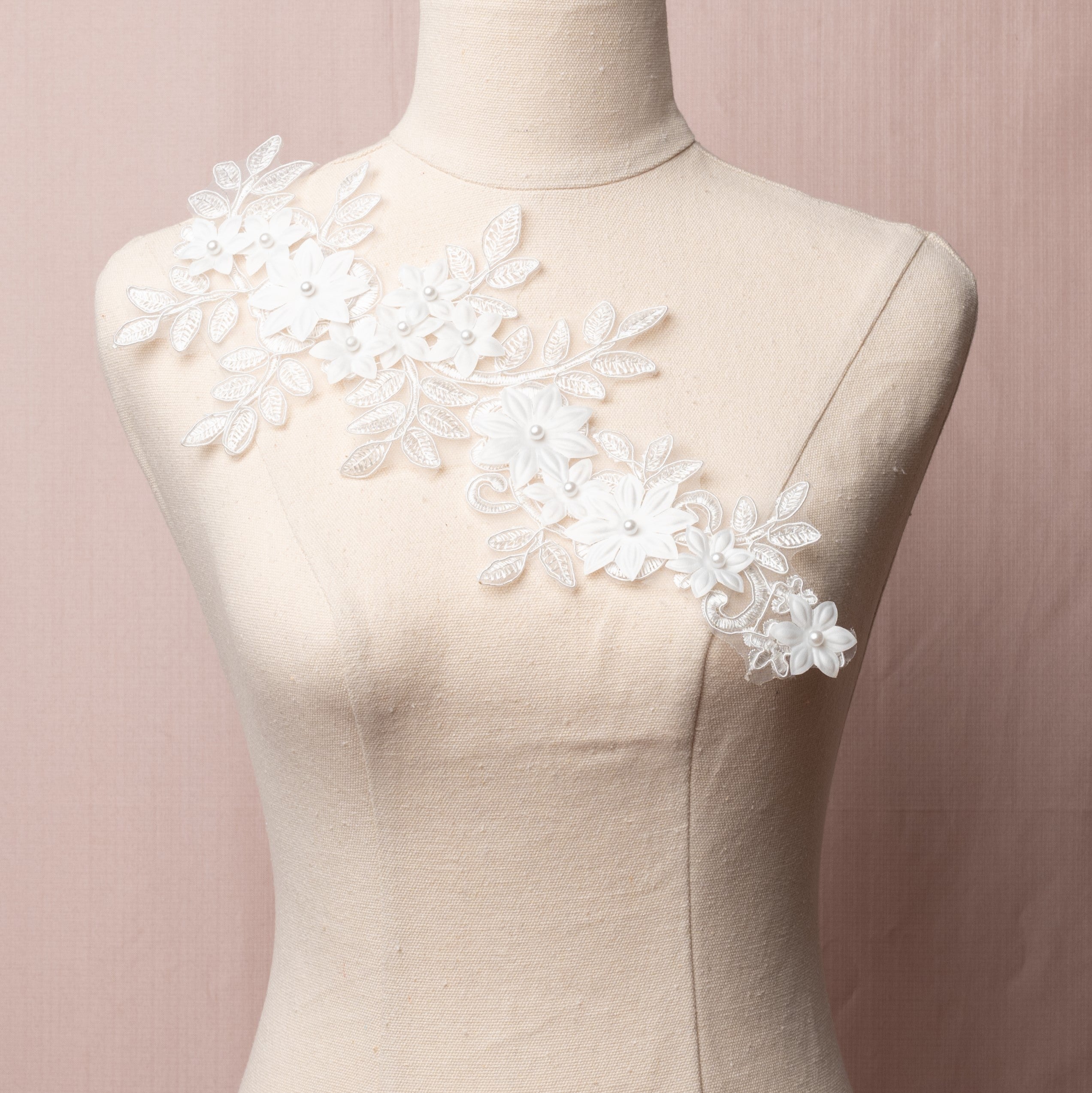 Single white corded floral applique embroidered onto an organza backing.  The applique is embellished with 3D fabric flowers that have a pearl centre.  The applique is displayed on the diagonal on a mannequin.