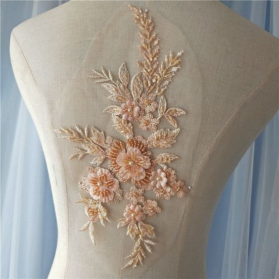 Heavily beaded apricot orange floral applique embroidered with a pale apricot thread  thread and embellished with darker apricot beads and 3D flower petals.  The applique is displayed on a mannequin.