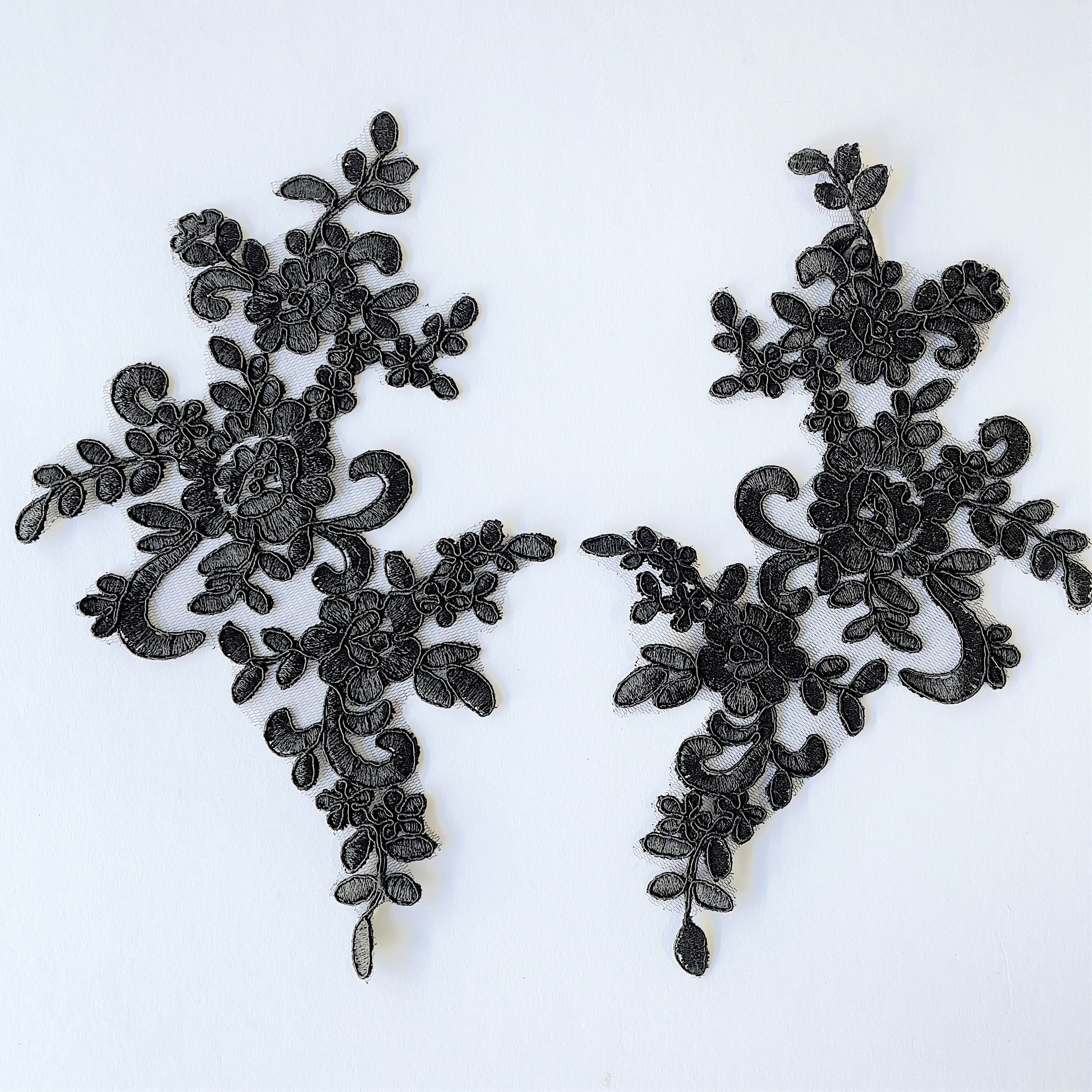A pair of black corded appliques in a floral design. laying flat on a white background.