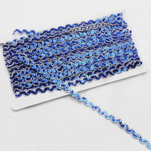Blue non-stretch sequins in a serpentine pattern edged with a metallic silver thread border.  The sequins are wrapped around a white card with a single strand lying flat across the image.