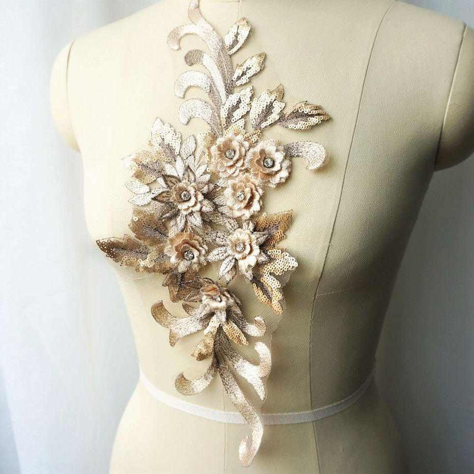 Single gold floral applique embroidered with metallic thread and embellished with sequinned leaves and 3D flowers that have a crystal centre.  The applique is displayed on a mannequin. 