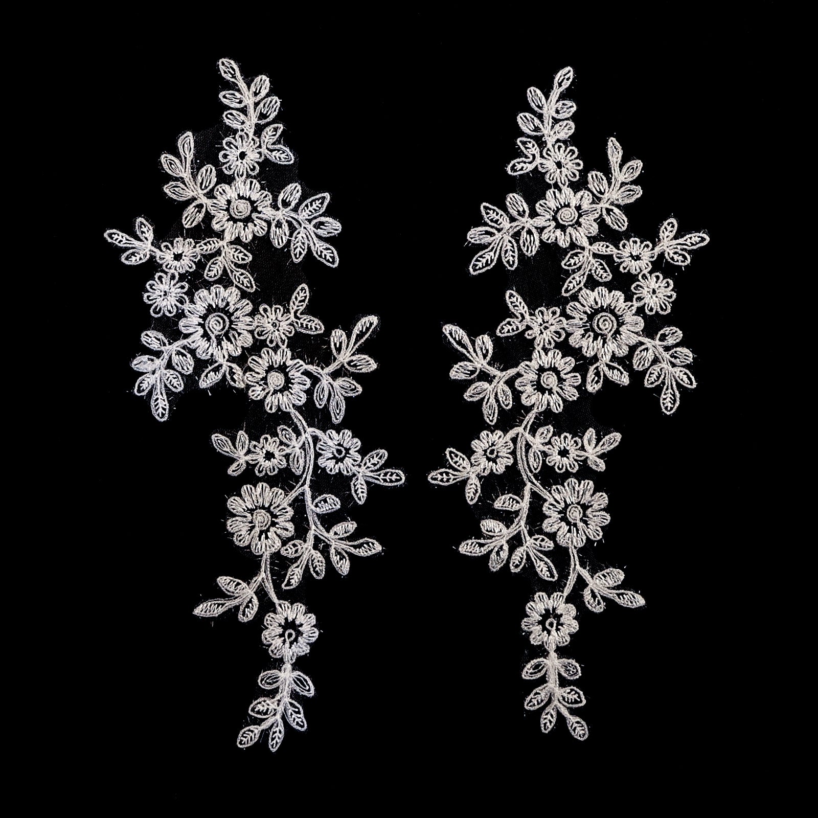 White floral applique embroidered with sparkly eye lash glitter thread.  The appliques are laying flat on a black background. 