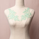 Mint green embroidered and corded applique pair with a floral design displayed on a mannequin.