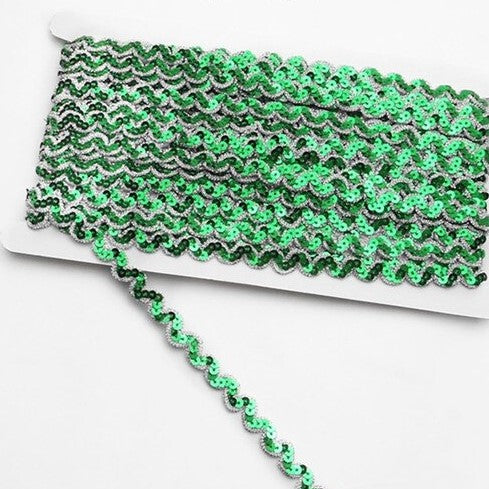 Green non-stretch sequins in a serpentine pattern edged with a metallic silver thread border.  The sequins are wrapped around a white card with a single strand lying flat across the image.