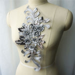 Single light grey blue floral applique embroidered with metallic thread and embellished with sequinned leaves and 3D flowers that have a crystal centre.  The applique is displayed on a mannequin. 