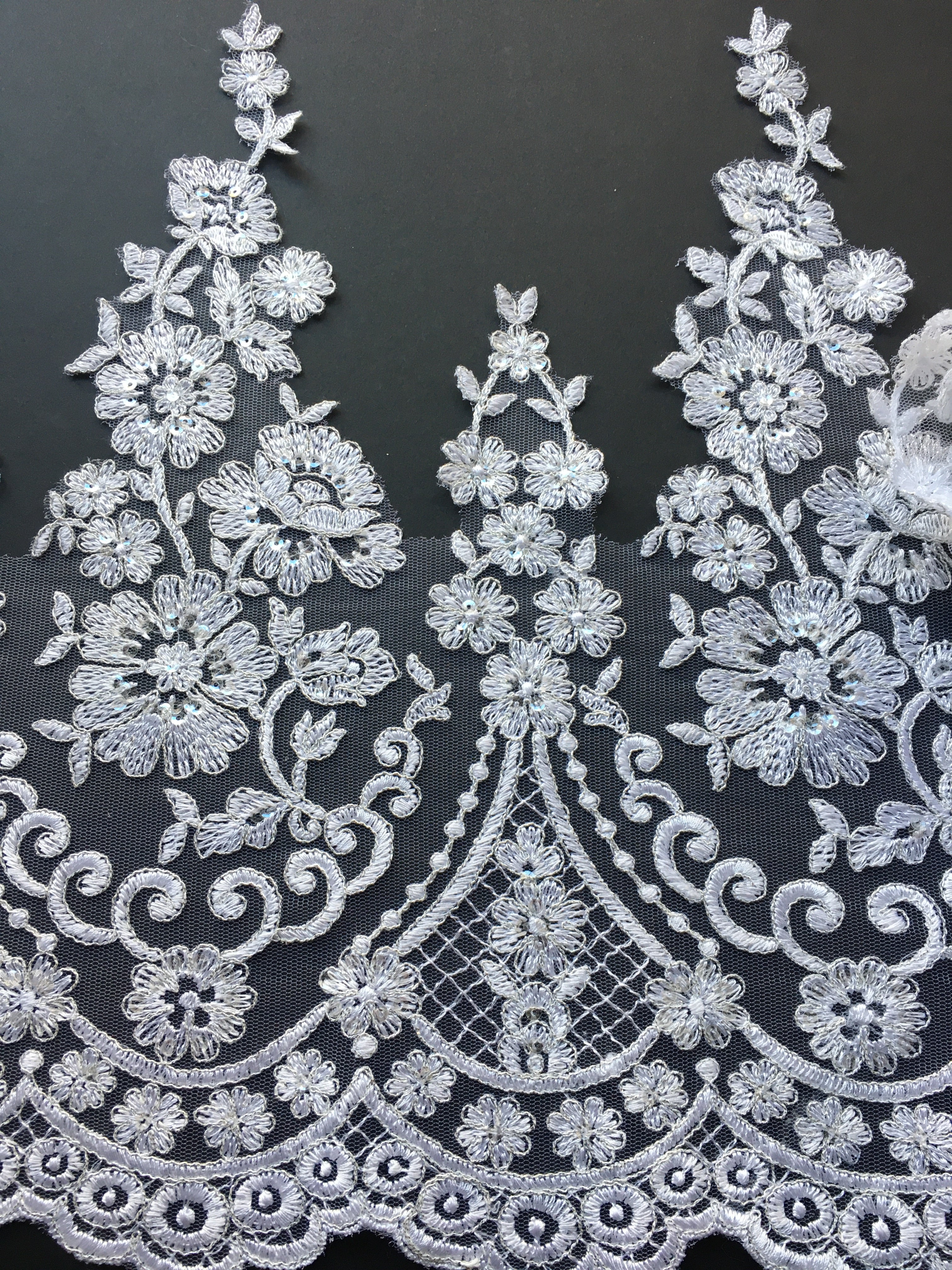 Stunning white lace with a floral pattern.  Each part of the design is outlined with silver thread and the flowers are embellished with silver sequins making the lace shimmer under lights.