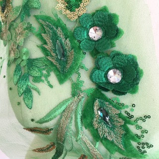 A close up view showing flower and leaf shapes embroidered with metallic thread and centres embellished with crystals and green horse eye gems..  