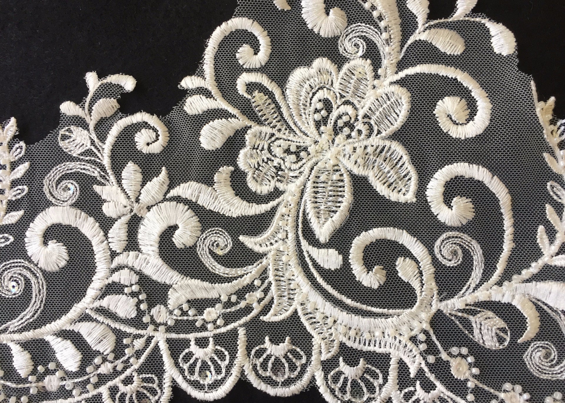 Delicate ivory embroidered lace with an asymmetrical scalloped border.  The border has petal shapes embroidered along the scallops.