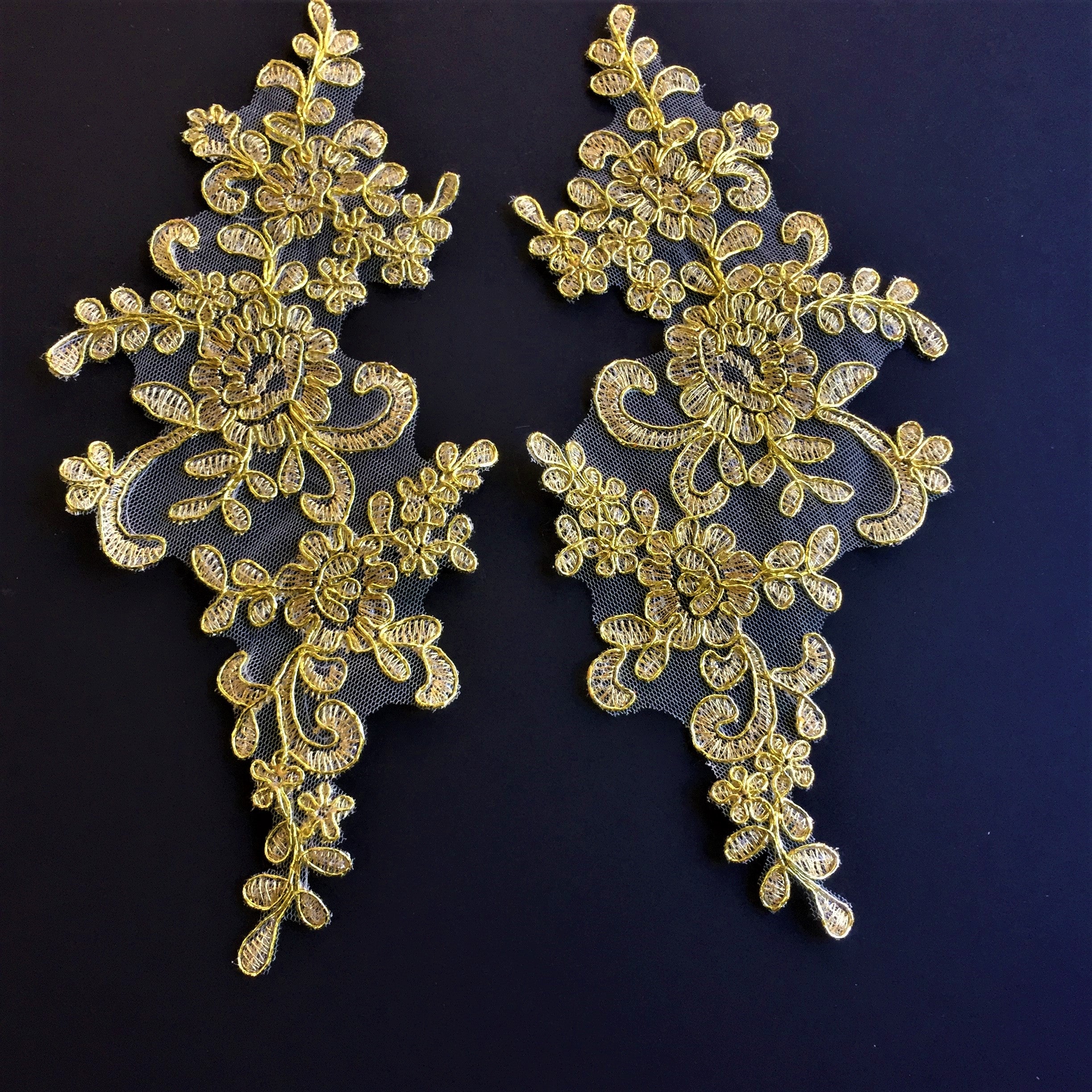 Gold floral embroidered applique pair laying flat on a blue background.  The applique is embroidered with non metallic gold coloured thread.  The flower stems and leaves are outlined with a metallic gold cord. 