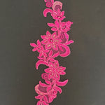 Single rose pink corded applique with  a floral design laying flat on a black background.  The applique is embroidered on a fine net backing and has silver thread and bead accents.