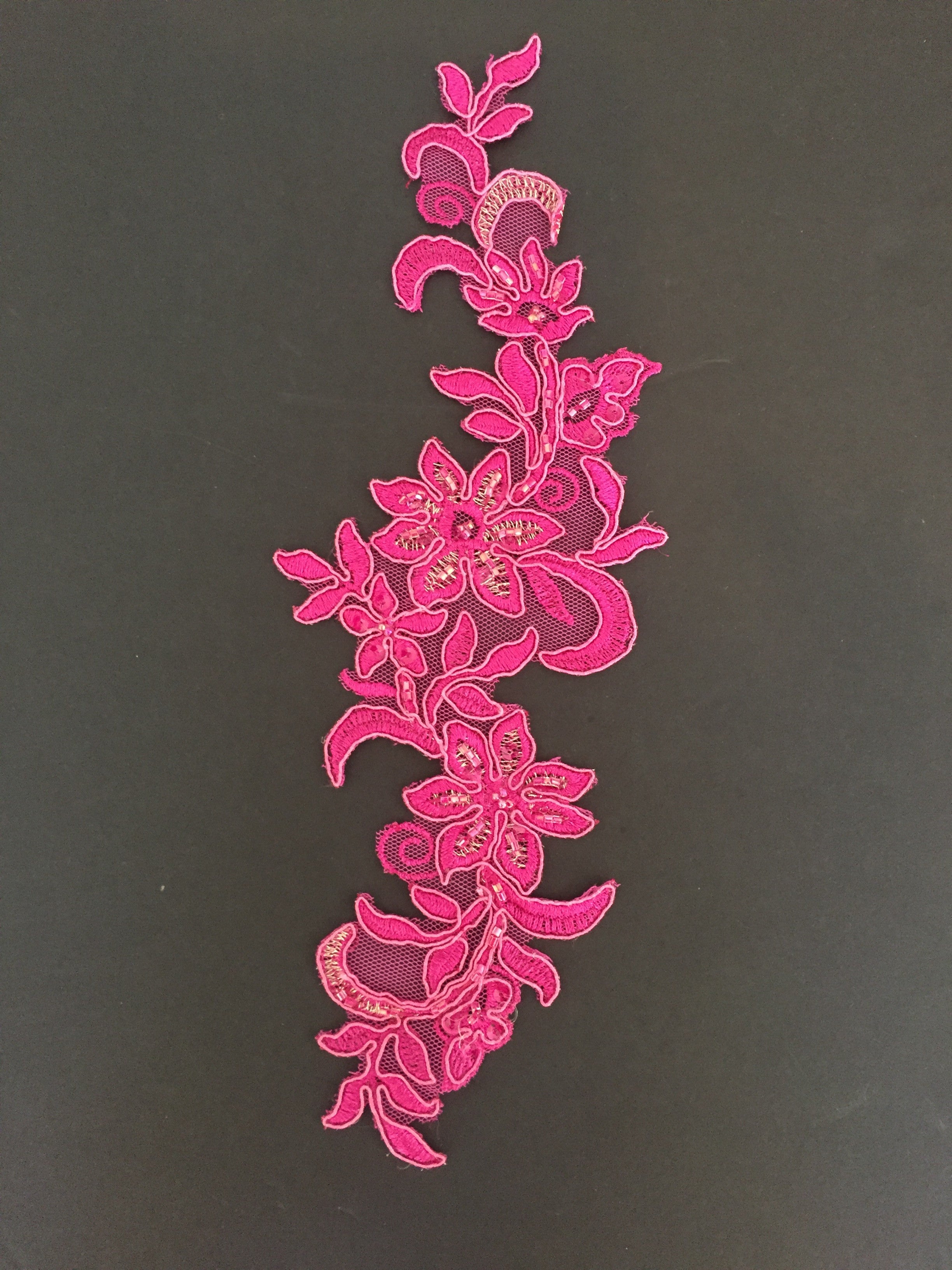 Single rose pink corded applique with  a floral design laying flat on a black background.  The applique is embroidered on a fine net backing and has silver thread and bead accents.