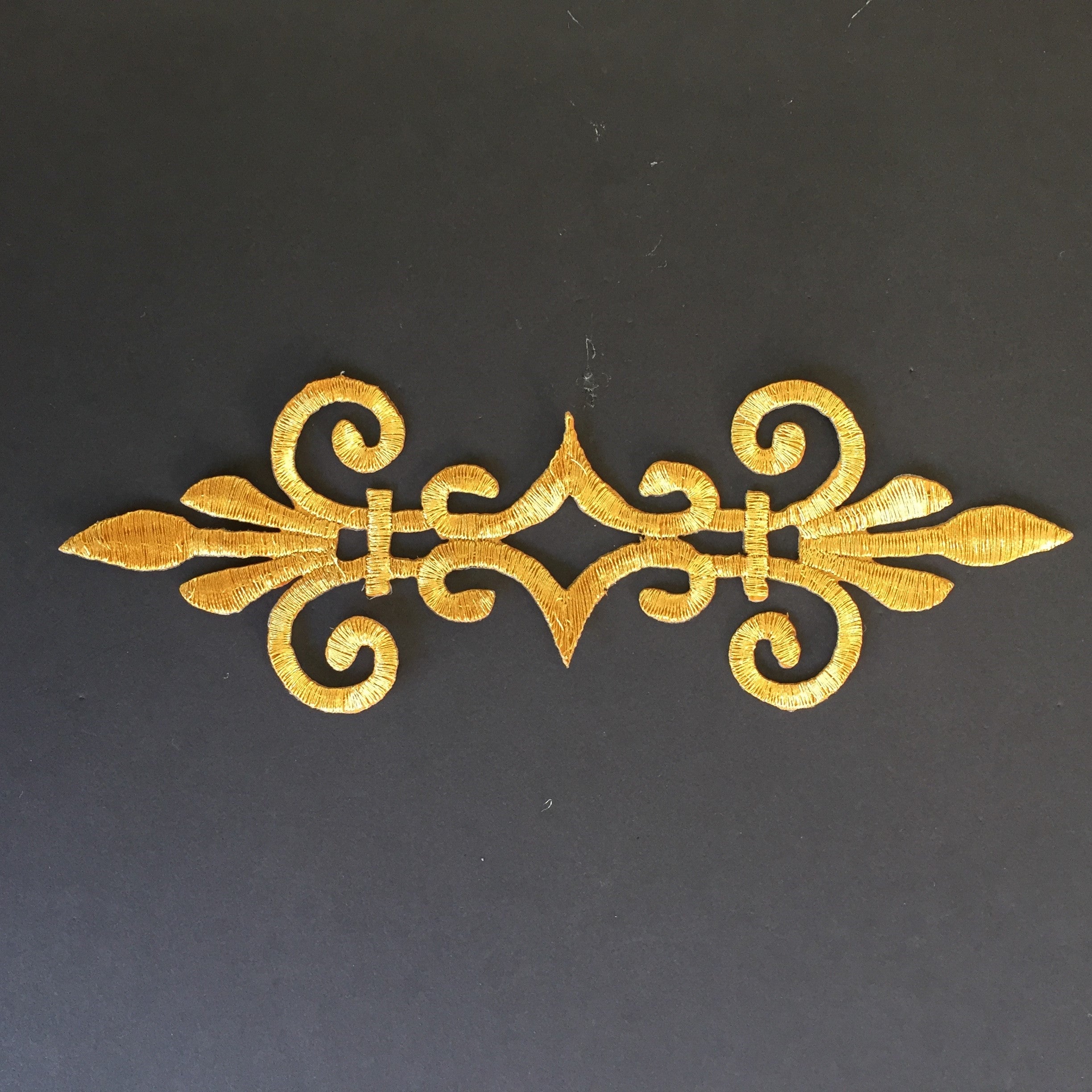 Metallic gold baroque style embroidered cosplay applique on a back background.