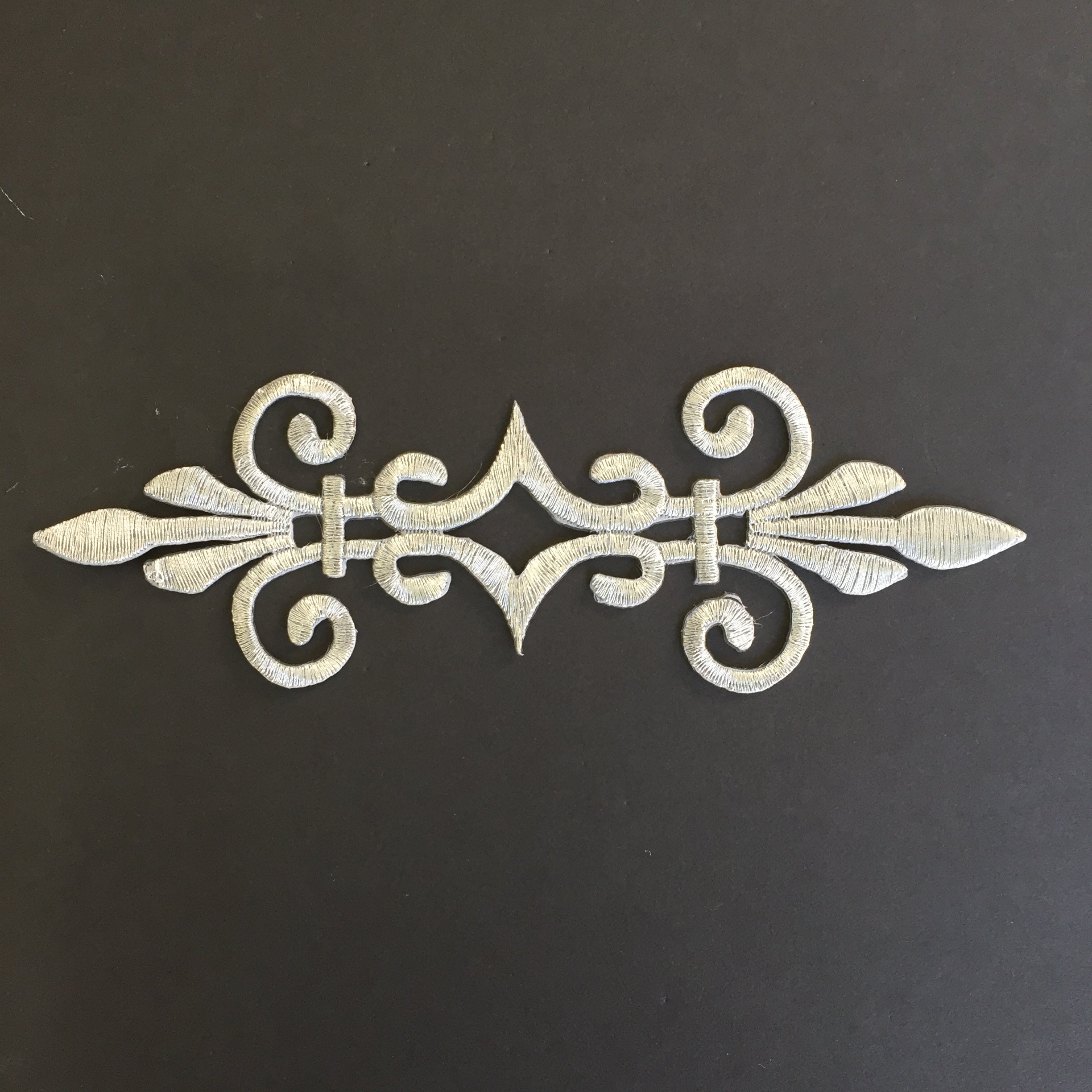 Single baroque style applique embroidered with metallic silver thread displayed on a black background.