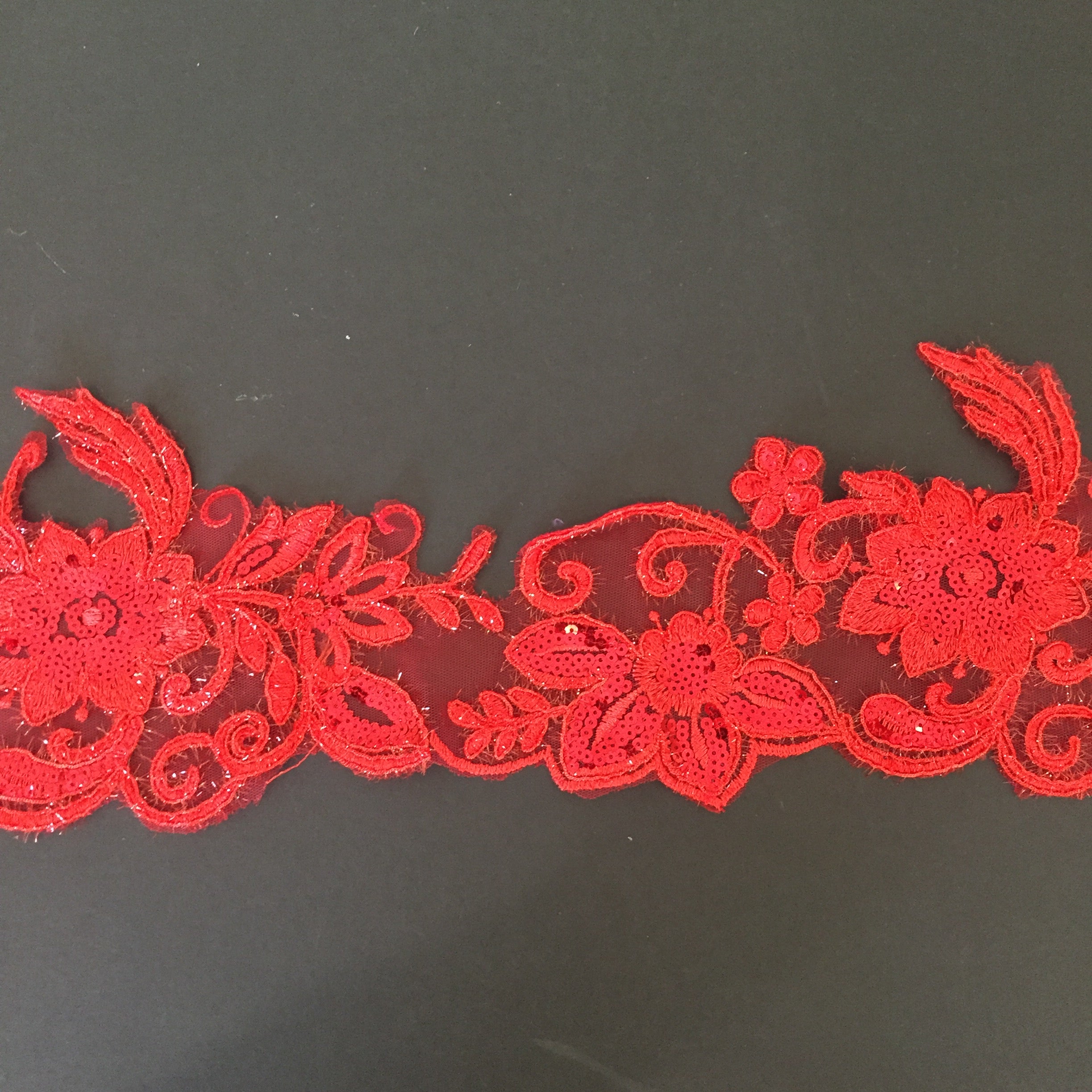 Red lace border with floral pattern and embellished with red sequins on flower centres and leaves.  Embroidered with glittery thread which sparkles under the light.