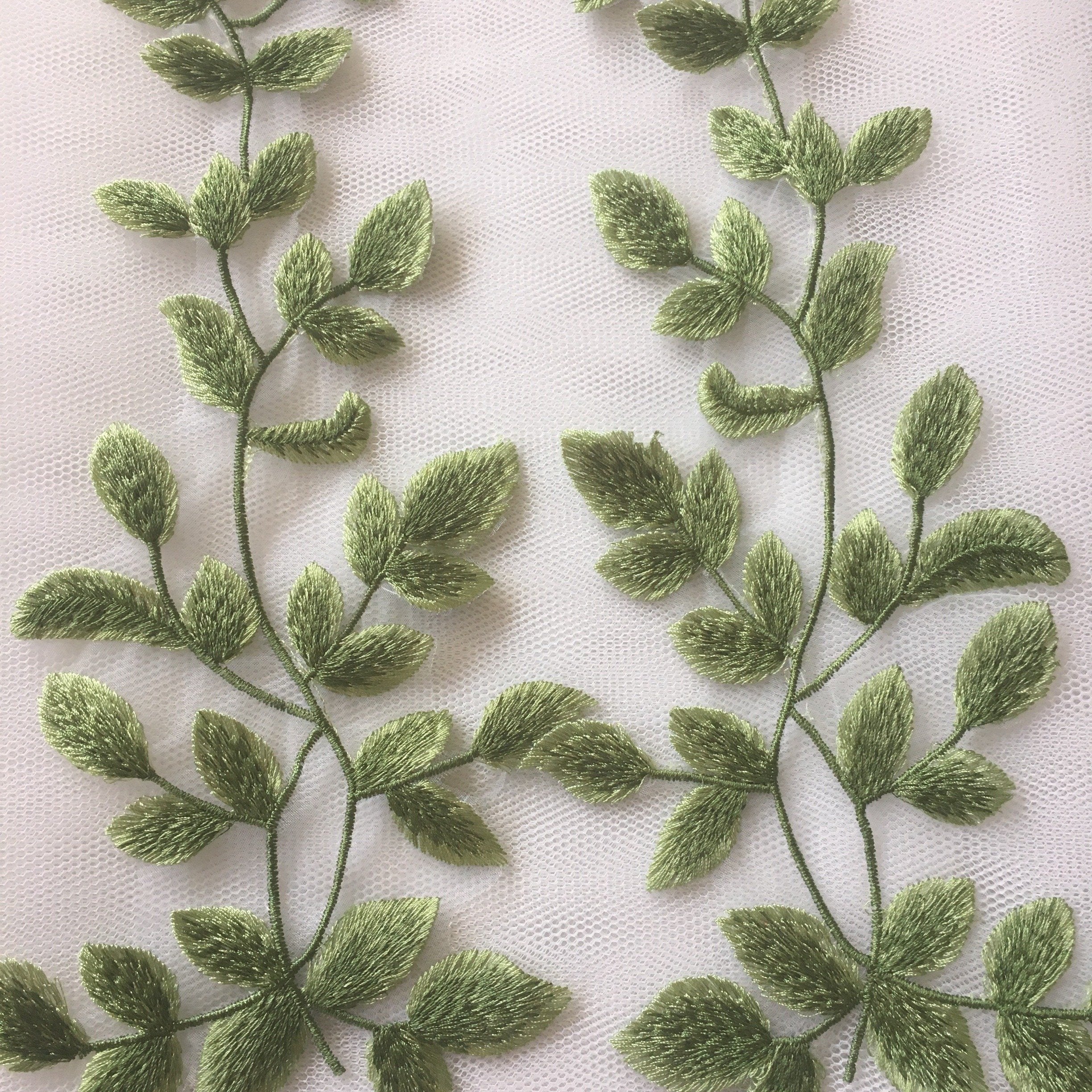 The mirrored pair of green leaves is embroidered onto a fine net backing with clusters of leaves coming from a fine tracery of stems . Leaf and stem motifs can be individually cut for adding to costumes such as Peter Pan , Woodland Fairy and Elf. 
