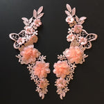 Pink embroidered lace applique pair decorated with 3D flowers that are embellished with beads and rhinestones.  Appliques are laying flat on a black background.