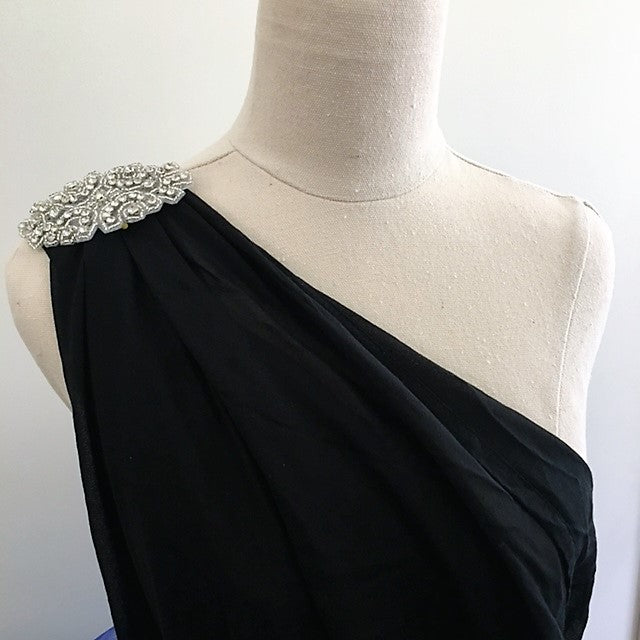 Crystal rhinestone applique  on the shoulder of a one shoulder black evening dress which is displayed on a mannequin.