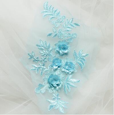 Single ice blue embroidered floral applique with 3D flowers laying on a white net background.