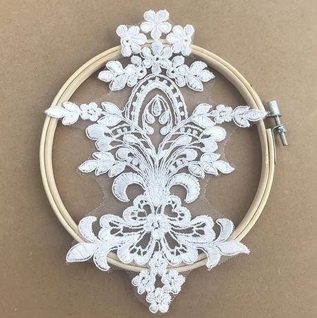 Ivory embroidered medallion shape applique  resting on an embroidery hoop.