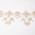 White embroidered lace trim with a large central medallion and two smaller medallions.  small and large medallion shapes that are edged with bright gold cord.
