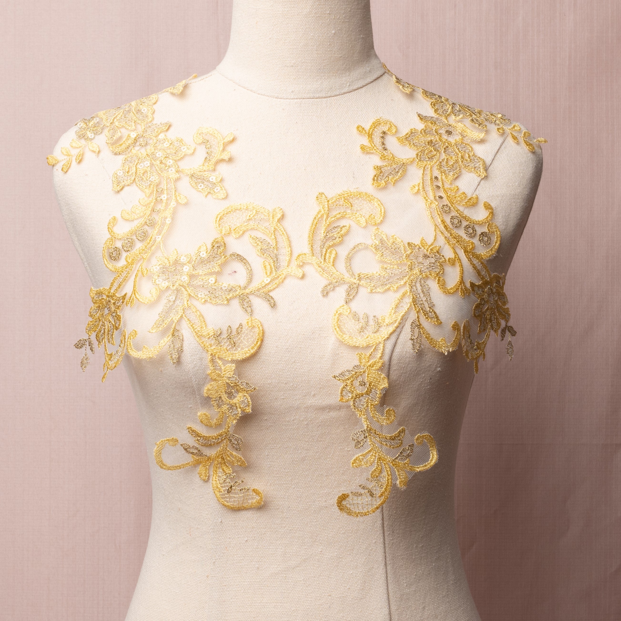 A golden yellow floral applique pair highlighted with gold thread on the leaves and flower petals.  The applique is embroidered onto a very fine net and sprinkled with clear sequins and is displayed on a mannequin.