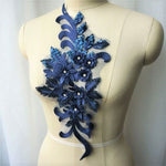 Single navy blue floral applique embroidered with metallic thread and embellished with sequinned leaves and 3D flowers that have a crystal centre.  The applique is displayed on a mannequin. 