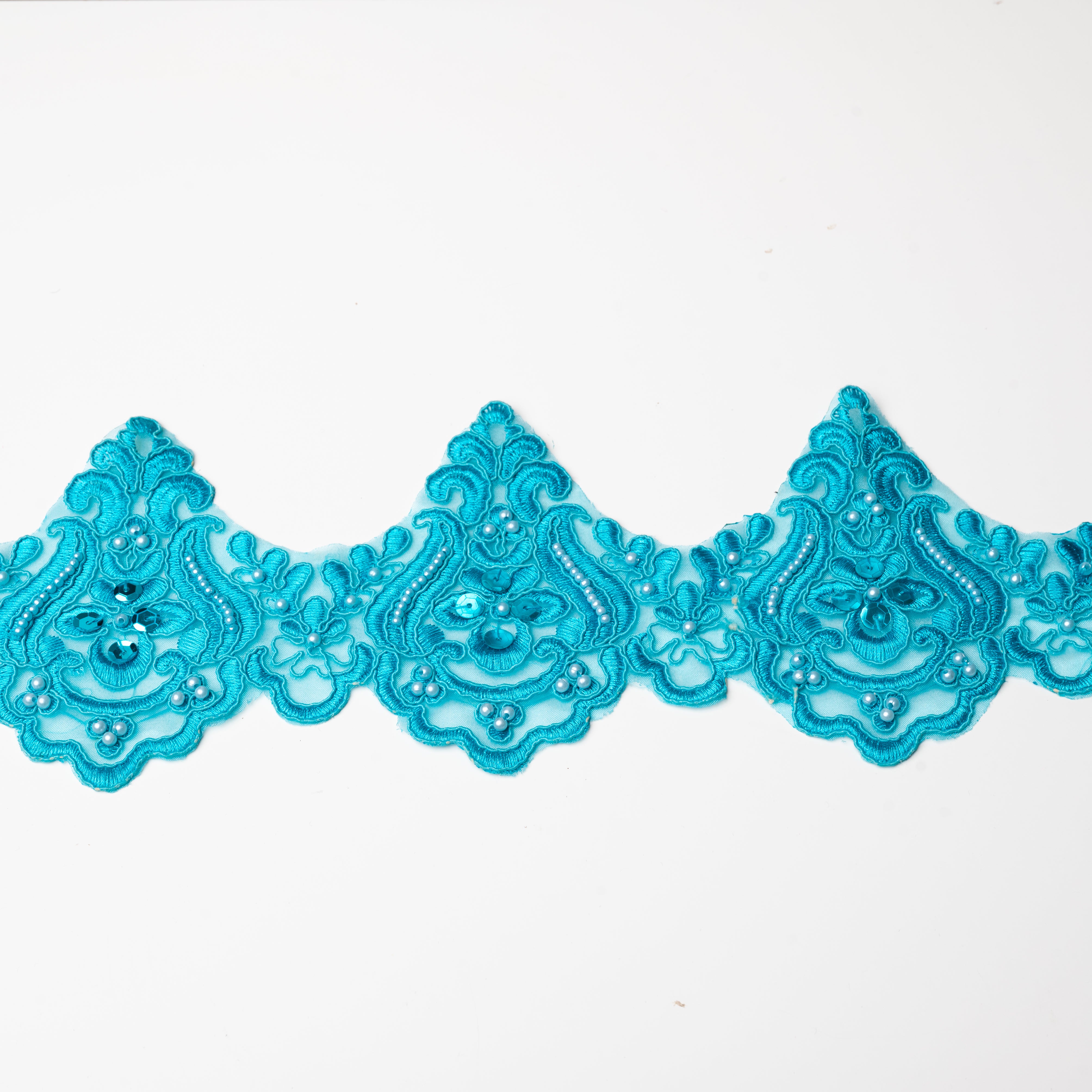 Turquoise blue scalloped lace embroidered onto an organza backing and embellished with pearls and sequins.  The lace is laying flat on a white background.