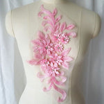 Single pink floral applique embroidered with metallic thread and embellished with sequinned leaves and 3D flowers that have a crystal centre.  The applique is displayed on a mannequin. 