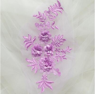 Single embroidered purple floral applique laying on a white net background.