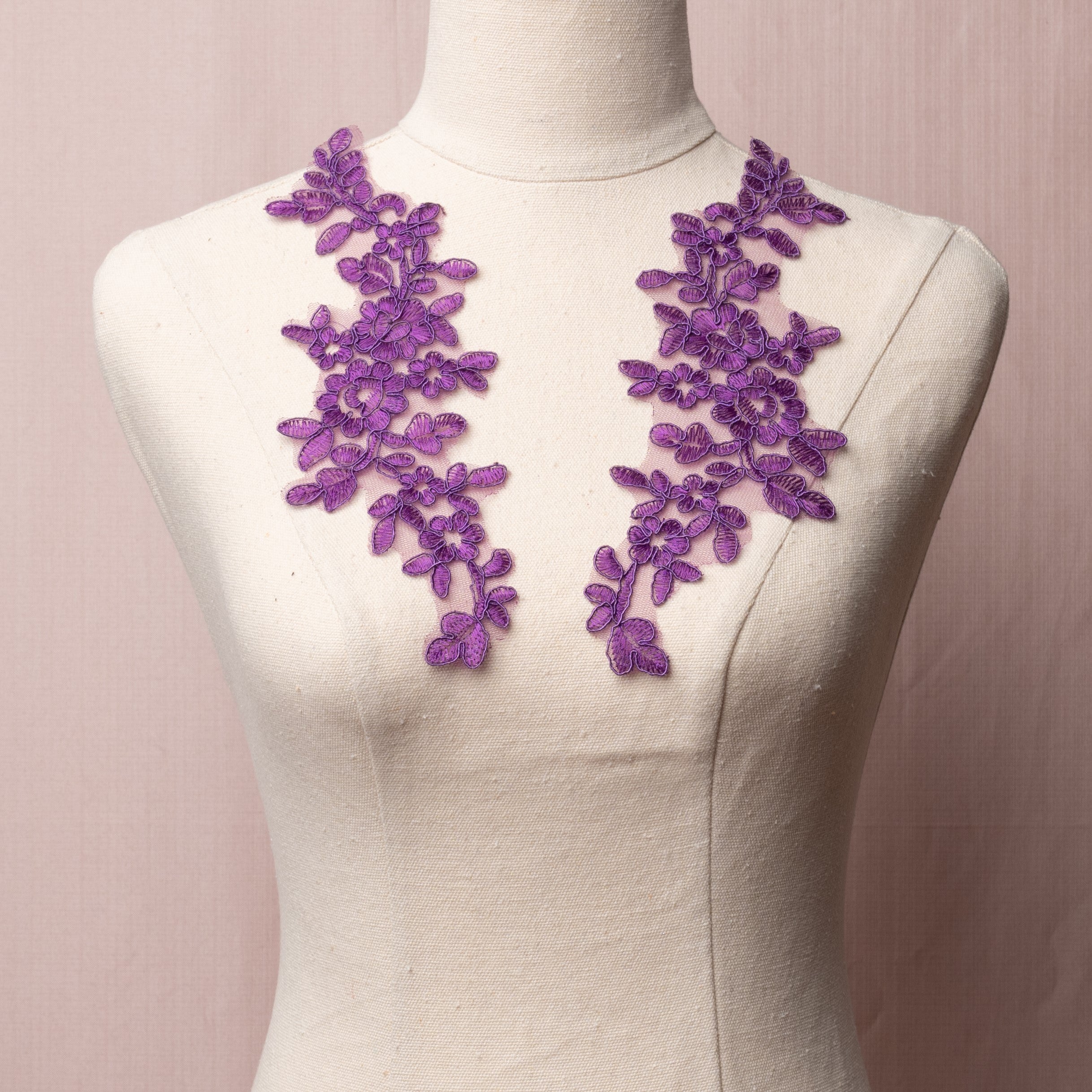 Mirrored purple corded appliques embroidered onto a fine net backing.  The appliques are displayed on a mannequin.