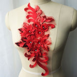 Single red floral applique embroidered with metallic thread and embellished with sequinned leaves and 3D flowers that have a crystal centre.  The applique is displayed on a mannequin. 