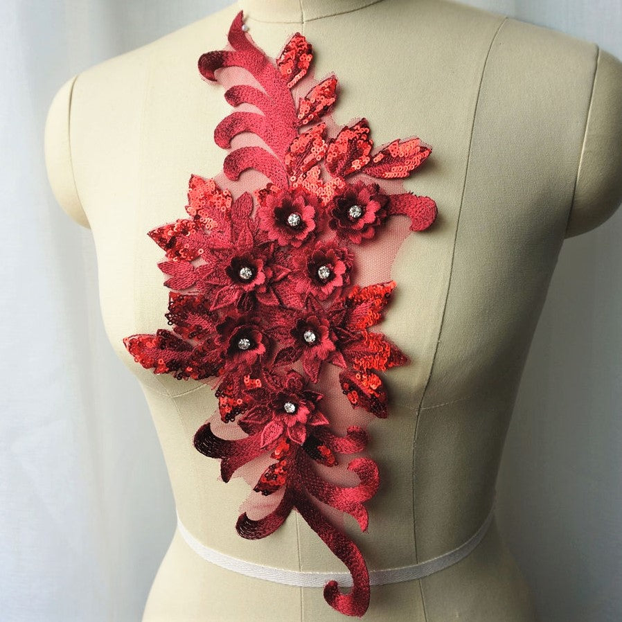 Single burgundy floral applique embroidered with metallic thread and embellished with sequinned leaves and 3D flowers that have a crystal centre.  The applique is displayed on a mannequin. 