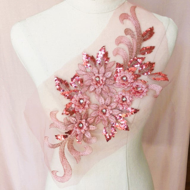 Single dusty pink floral applique embroidered with metallic thread and embellished with sequinned leaves and 3D flowers that have a crystal centre.  The applique is displayed on a mannequin. 