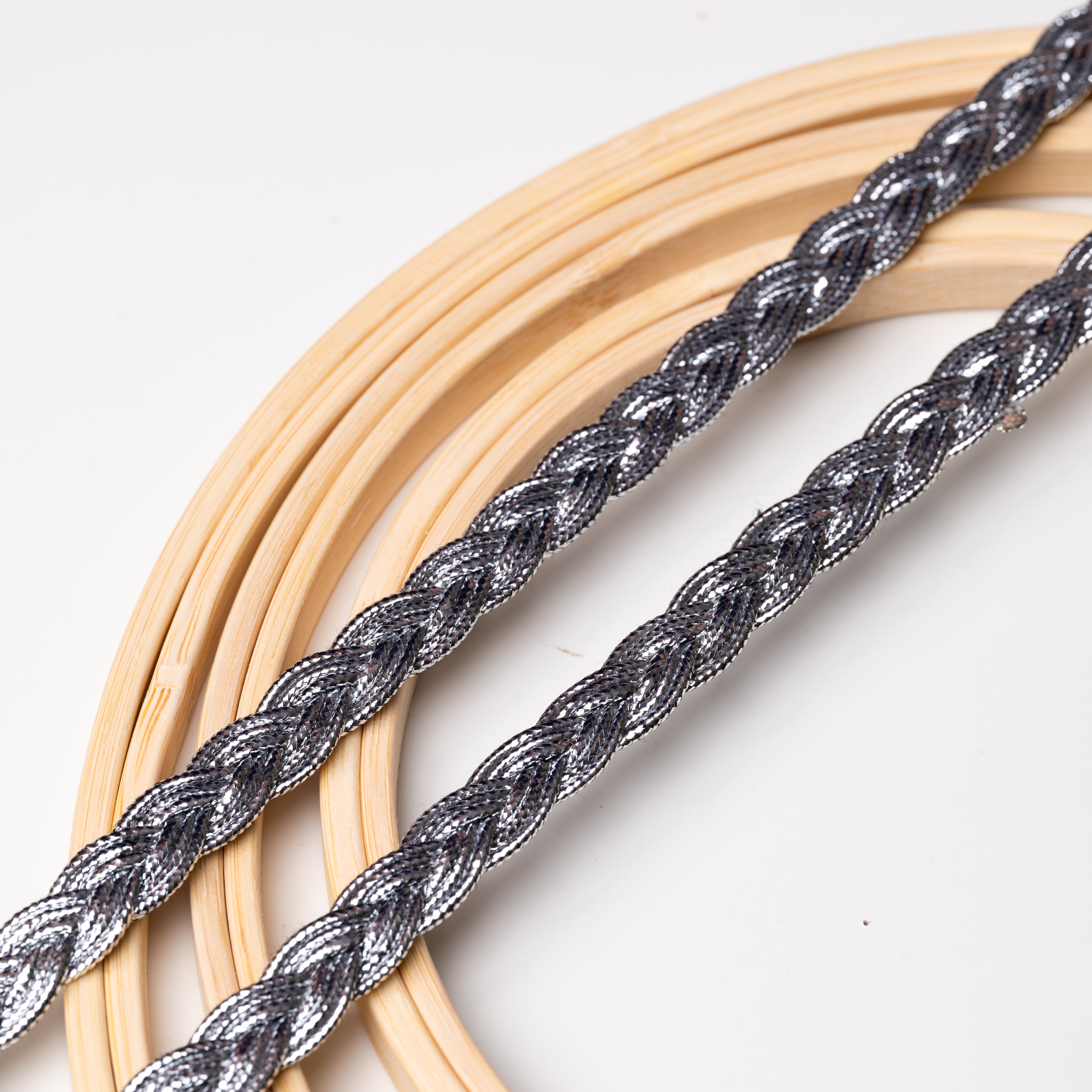 Silver metallic trim in a braided pattern laying flat across wooden embroidery rings.