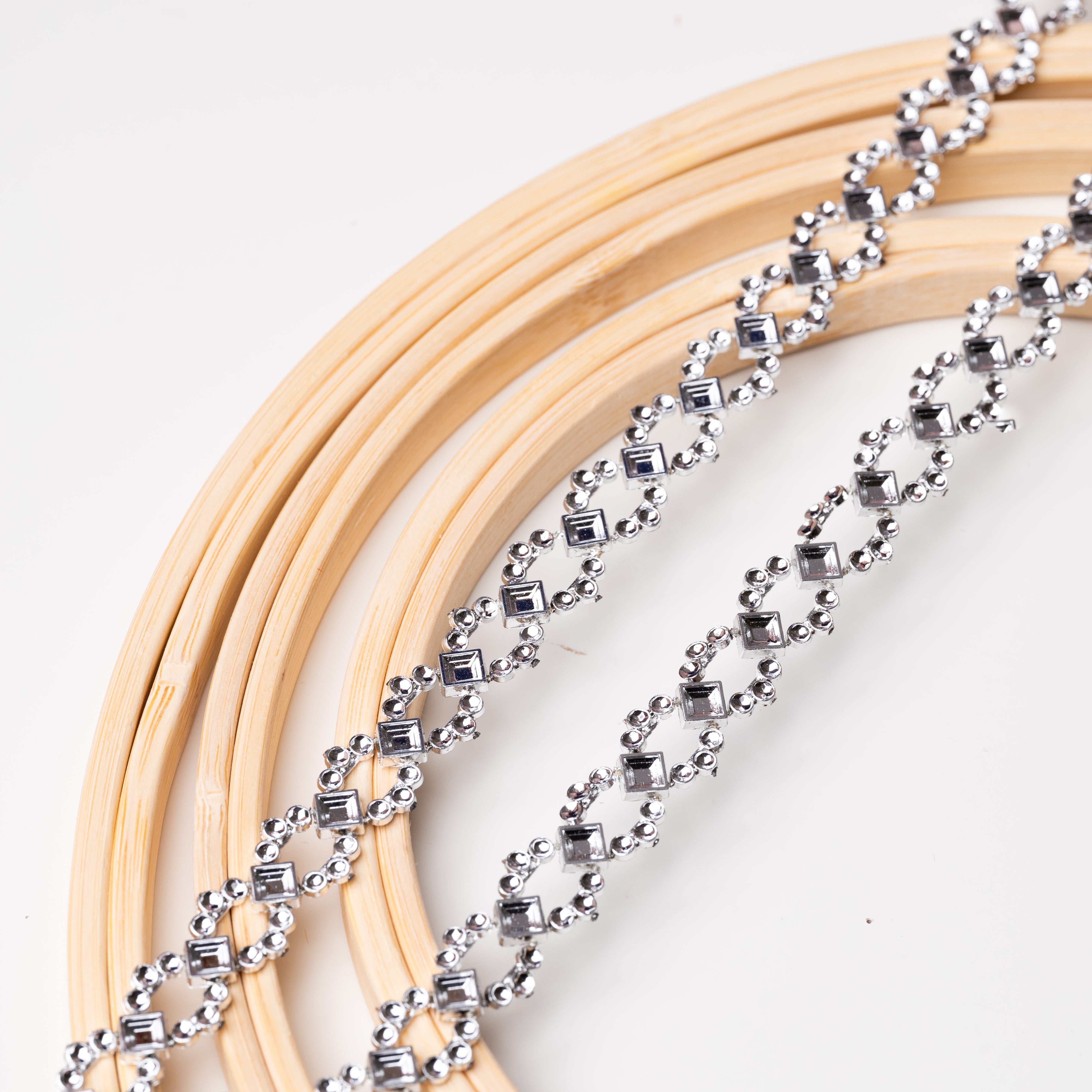 Silver diamante chain trim laying flat across wooden embroidery rings.