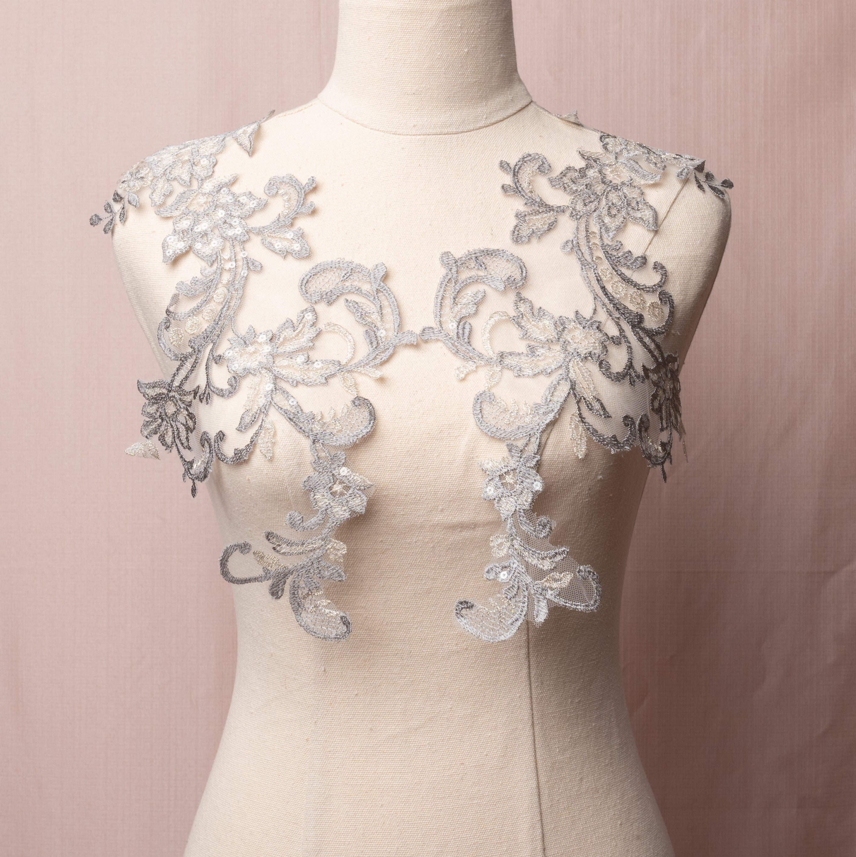 A delicate grey floral applique highlighted with silver thread on the leaves and flower petals.  The applique is embroidered onto a very fine net and sprinkled with clear sequins.   The appliques are displayed on a mannequin.
