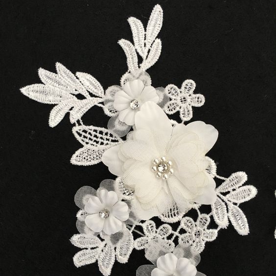 Close up of white embroidered floral applique with one large and three smaller 3D fabric flowers.  The fabric flowers have crystal centres circled with pearl beads.