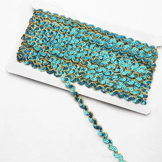 Turquoise non-stretch sequins in a serpentine pattern edged with a metallic gold thread border.  the sequins are wrapped around a white card with a single strand lying flat across the image.